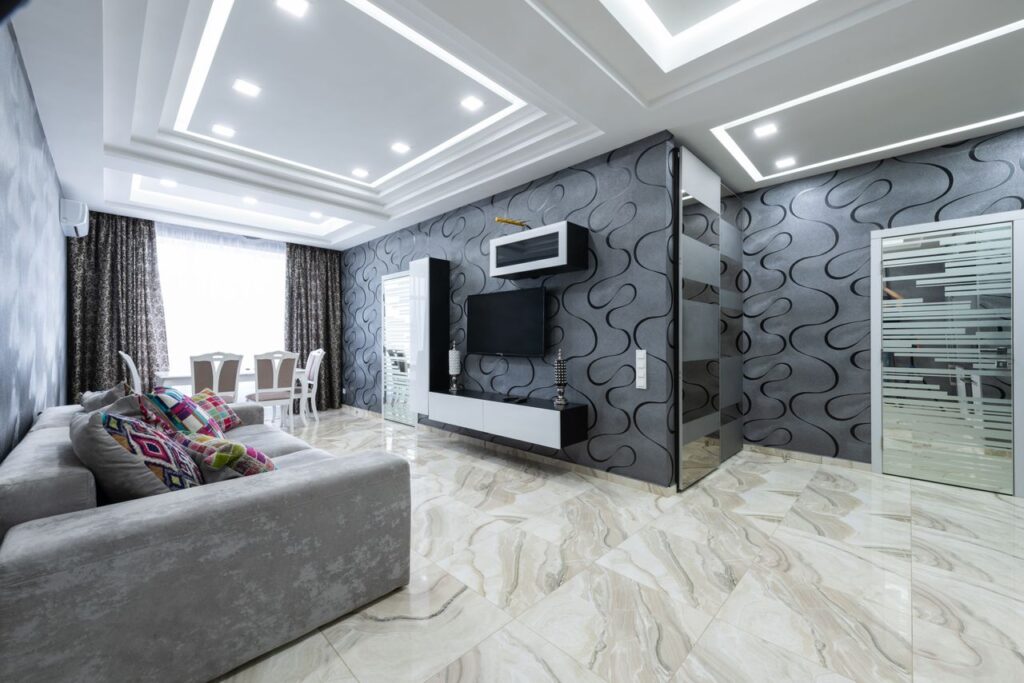 Comfortable gray sofa with pillows placed opposite TV in living room with gray walls in contemporary apartment in daylight